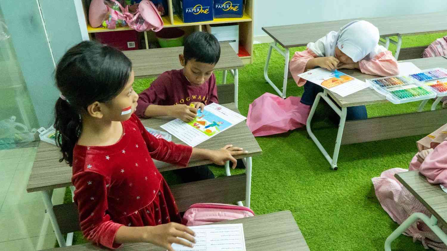Seorang anak fokus memegang kuas melukis pemandangan warna-warni di atas meja